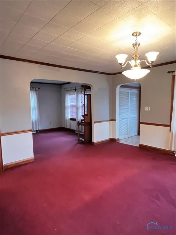 spare room featuring crown molding, carpet, and a chandelier