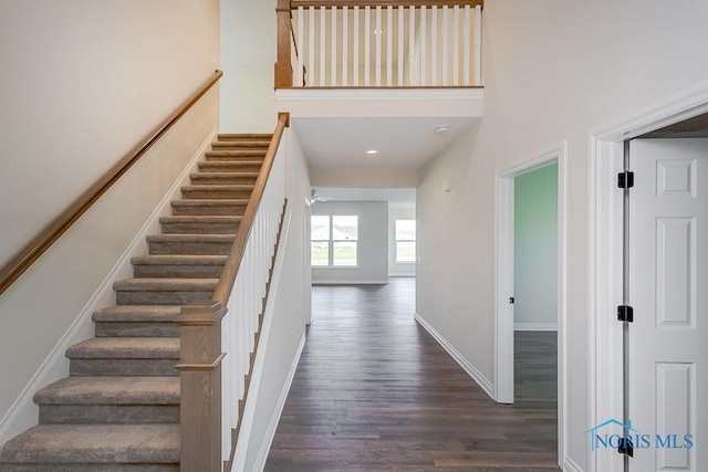 stairs featuring ceiling fan, wood-type flooring, and a towering ceiling