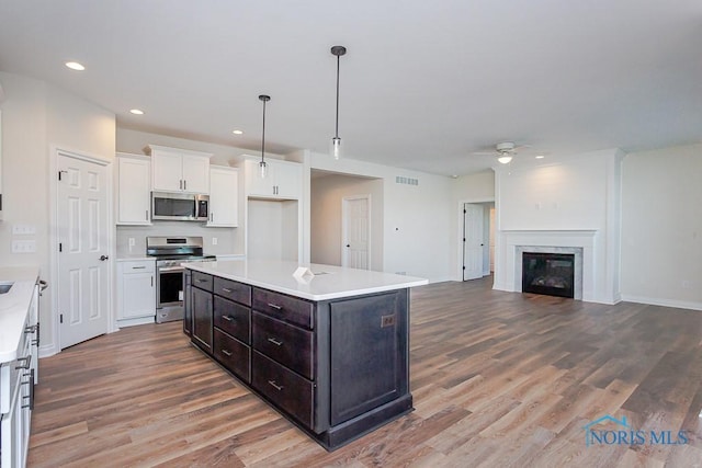 kitchen featuring a kitchen island, wood-type flooring, a fireplace, white cabinets, and appliances with stainless steel finishes