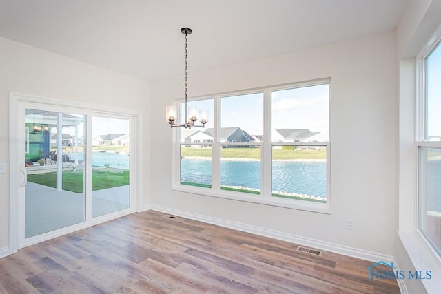 unfurnished dining area featuring a water view, a chandelier, and hardwood / wood-style flooring