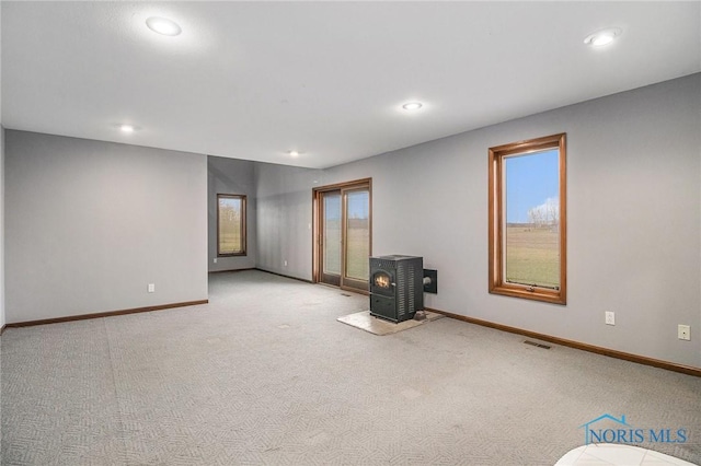 spare room featuring a wood stove, light carpet, and a healthy amount of sunlight