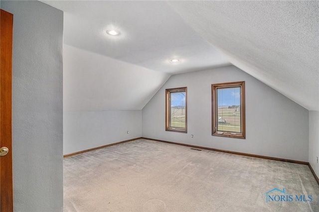 bonus room featuring a textured ceiling, light colored carpet, and lofted ceiling