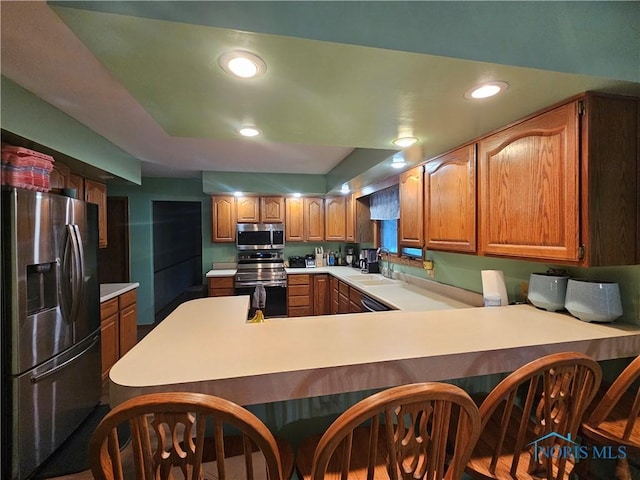 kitchen featuring sink, kitchen peninsula, a breakfast bar, appliances with stainless steel finishes, and hardwood / wood-style flooring