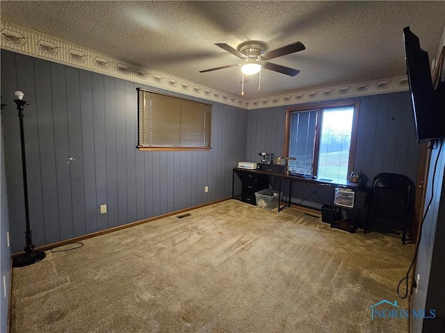 carpeted home office with a textured ceiling, ceiling fan, and wooden walls