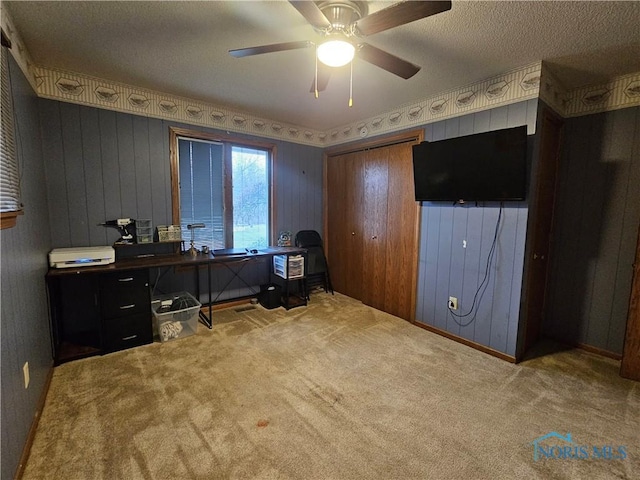 carpeted office space featuring a textured ceiling, ceiling fan, and wooden walls