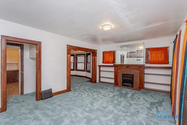 unfurnished living room featuring a fireplace, light colored carpet, and a textured ceiling