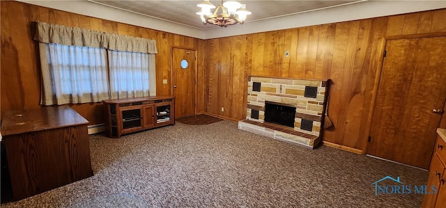 living room with baseboard heating, a chandelier, wooden walls, a fireplace, and dark carpet