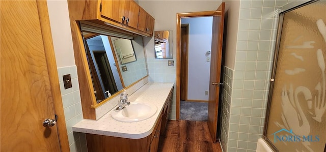 bathroom with shower / bath combination with glass door, vanity, hardwood / wood-style flooring, and tile walls