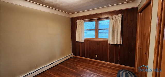 spare room with wood walls, dark hardwood / wood-style flooring, and a baseboard heating unit