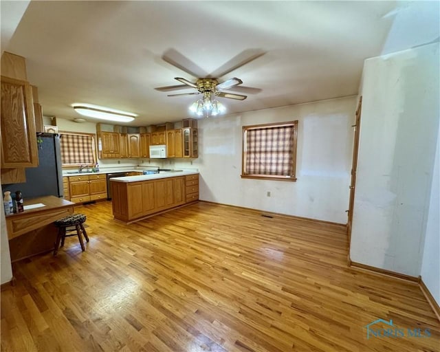 kitchen with ceiling fan, sink, black fridge, kitchen peninsula, and light hardwood / wood-style floors