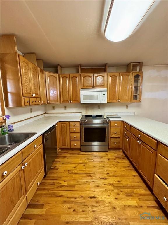 kitchen featuring sink, black dishwasher, light hardwood / wood-style floors, and stainless steel range oven