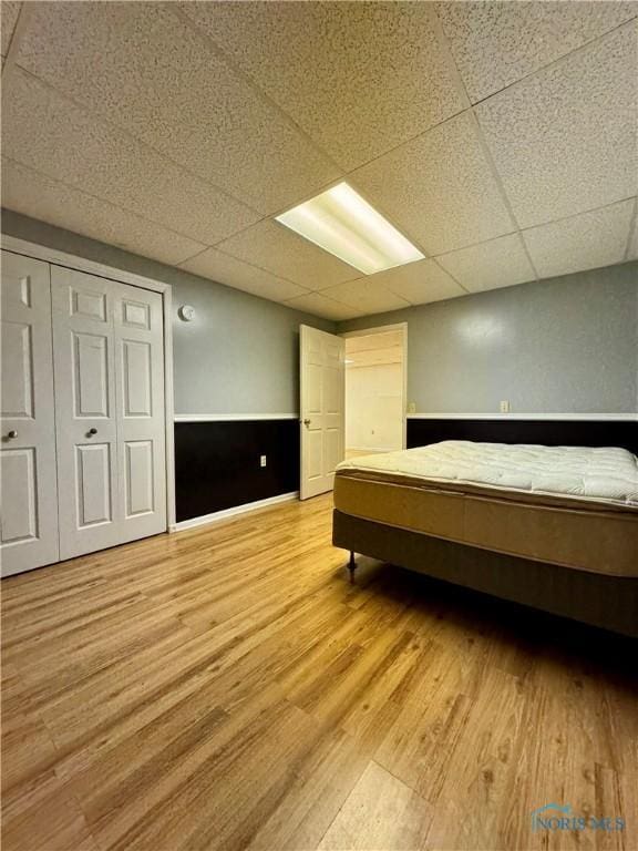 unfurnished bedroom featuring light wood-type flooring, a paneled ceiling, and a closet