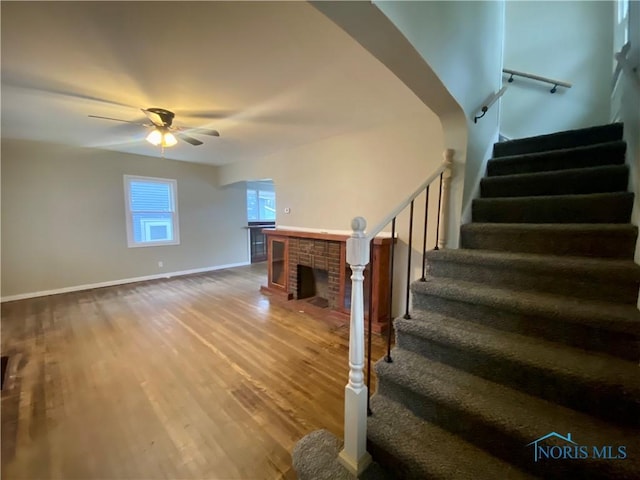 stairway featuring ceiling fan, a fireplace, and hardwood / wood-style flooring