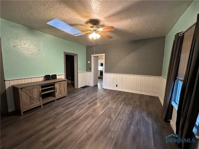 unfurnished bedroom with a skylight, ceiling fan, dark hardwood / wood-style flooring, and a textured ceiling