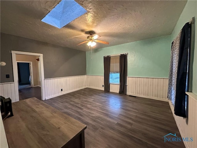 empty room with ceiling fan, dark hardwood / wood-style flooring, a textured ceiling, and a skylight