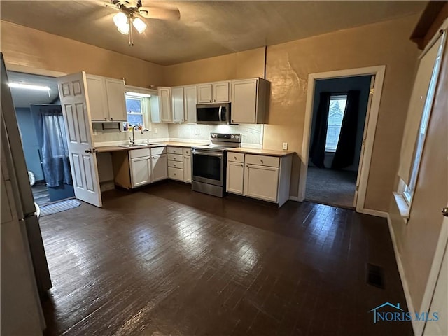 kitchen with white cabinets, appliances with stainless steel finishes, dark hardwood / wood-style floors, and a healthy amount of sunlight