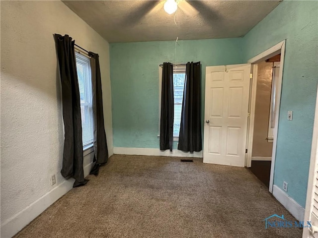 unfurnished bedroom with ceiling fan, carpet floors, a textured ceiling, and multiple windows