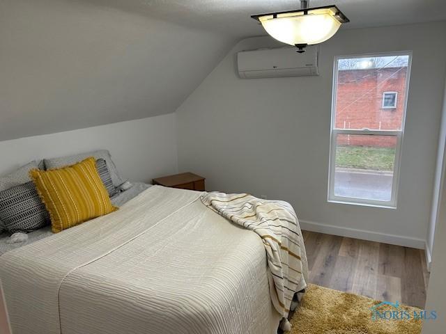 bedroom featuring hardwood / wood-style flooring, an AC wall unit, and lofted ceiling