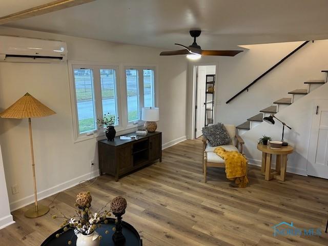 living area with hardwood / wood-style flooring, an AC wall unit, and ceiling fan