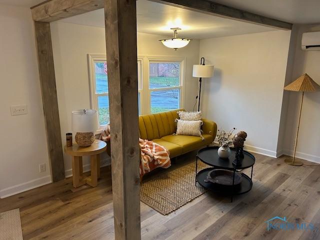 sitting room featuring a wall mounted air conditioner, beam ceiling, and hardwood / wood-style flooring