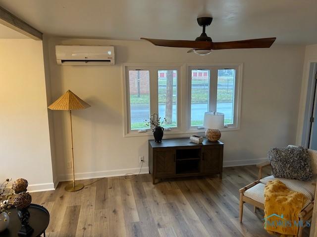 living area featuring a wall mounted air conditioner, ceiling fan, and light wood-type flooring