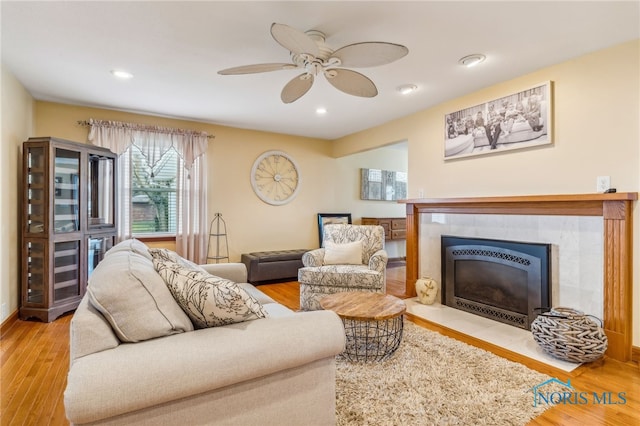 living room with a tile fireplace, light hardwood / wood-style flooring, and ceiling fan