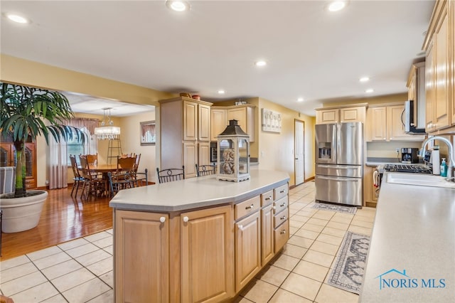 kitchen featuring appliances with stainless steel finishes, light brown cabinets, a center island with sink, light hardwood / wood-style flooring, and hanging light fixtures