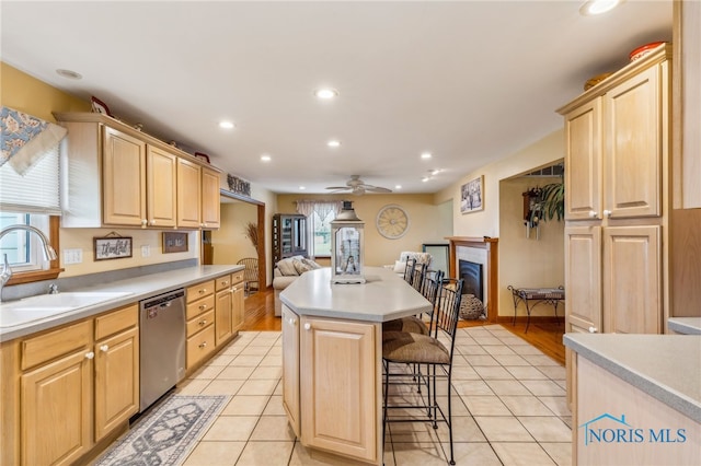 kitchen featuring light brown cabinetry, a center island, stainless steel dishwasher, and sink