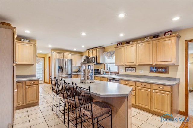 kitchen with light brown cabinetry, stainless steel appliances, light tile patterned floors, a center island, and a breakfast bar area