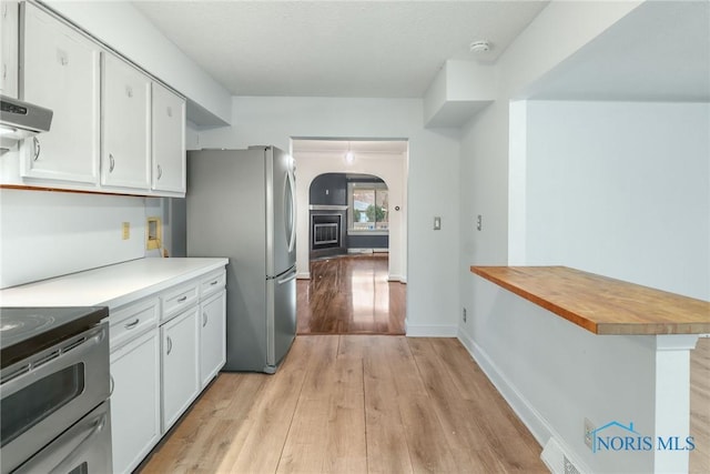 kitchen with stainless steel refrigerator, white cabinetry, light hardwood / wood-style floors, extractor fan, and range