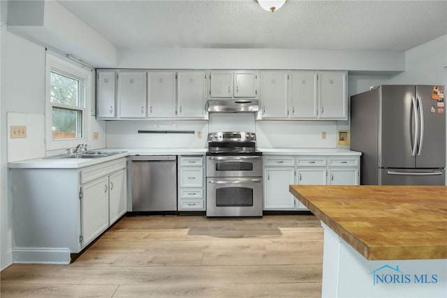 kitchen with wood counters, light wood-type flooring, a textured ceiling, stainless steel appliances, and sink