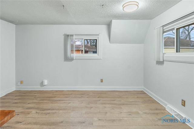 bonus room featuring lofted ceiling, light hardwood / wood-style floors, and a textured ceiling