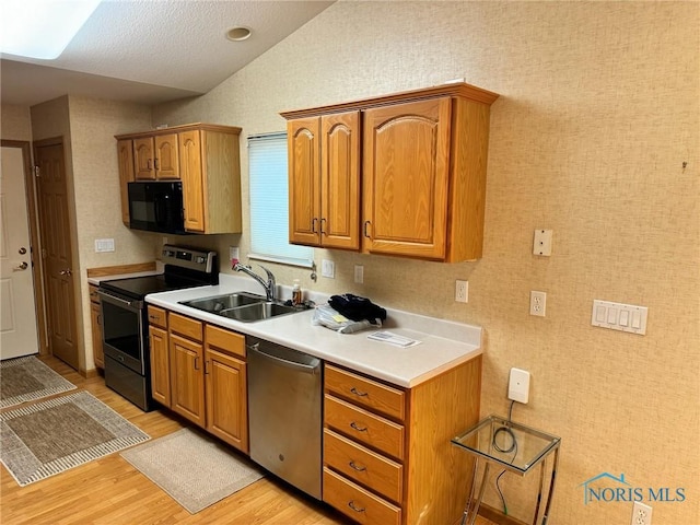 kitchen featuring black appliances, vaulted ceiling, sink, and light hardwood / wood-style flooring