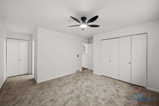 unfurnished bedroom with ceiling fan, light colored carpet, and two closets