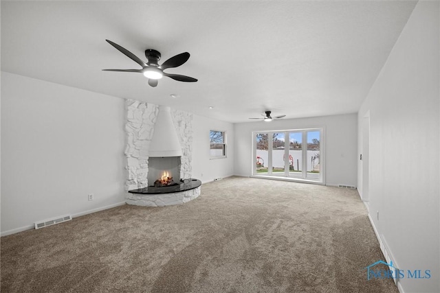 unfurnished living room featuring carpet floors, a stone fireplace, and ceiling fan