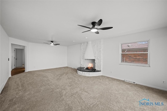 unfurnished living room featuring ceiling fan, a large fireplace, and carpet