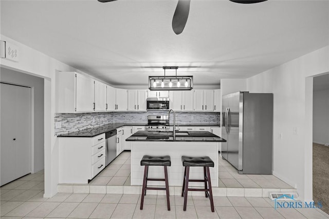 kitchen featuring white cabinetry, decorative backsplash, a center island with sink, light tile patterned floors, and appliances with stainless steel finishes