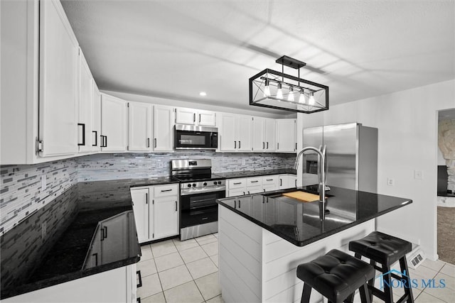 kitchen with white cabinets, light tile patterned floors, appliances with stainless steel finishes, a kitchen island, and a kitchen bar