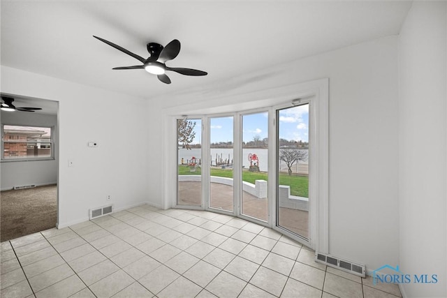 carpeted empty room featuring ceiling fan and a water view