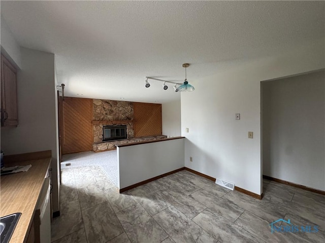 kitchen with a stone fireplace, sink, hanging light fixtures, rail lighting, and wooden walls