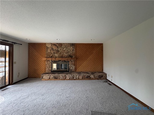 unfurnished living room with a stone fireplace, wood walls, and carpet floors