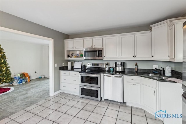 kitchen featuring white cabinets, sink, dark stone countertops, light tile patterned floors, and stainless steel appliances