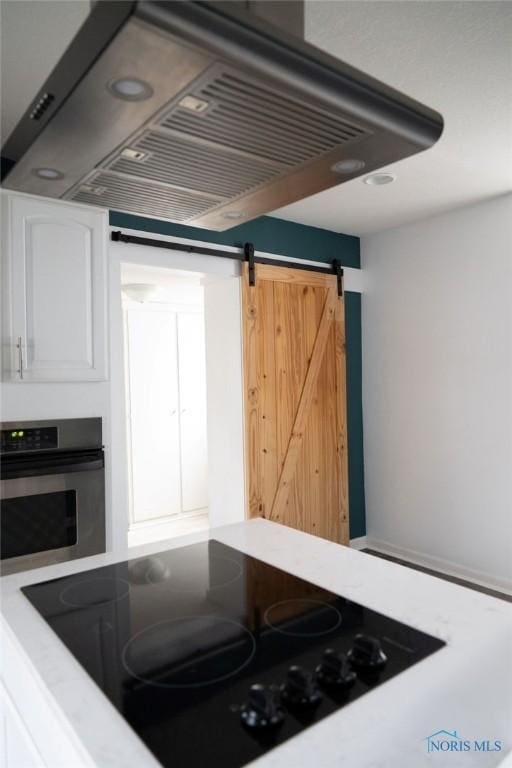 kitchen featuring a barn door, white cabinetry, stainless steel oven, and extractor fan