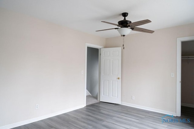 unfurnished bedroom featuring ceiling fan, wood-type flooring, a walk in closet, and a closet