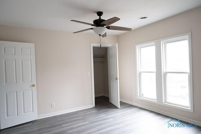 unfurnished bedroom with ceiling fan, light hardwood / wood-style floors, a walk in closet, and a closet