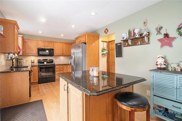 kitchen with decorative backsplash, dark stone counters, black appliances, light hardwood / wood-style flooring, and a kitchen island