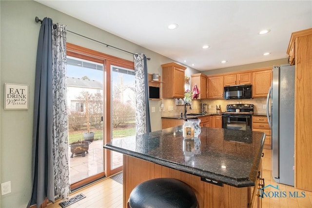 kitchen with dark stone countertops, a wealth of natural light, a kitchen island, and black appliances