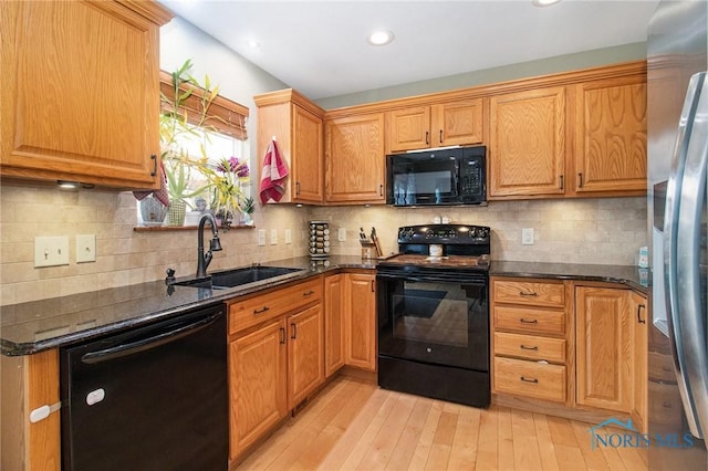 kitchen featuring black appliances, light hardwood / wood-style floors, sink, and dark stone counters