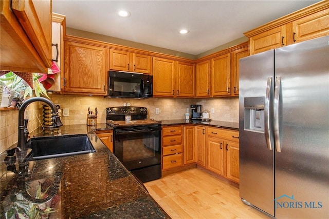 kitchen with backsplash, dark stone counters, sink, black appliances, and light hardwood / wood-style flooring