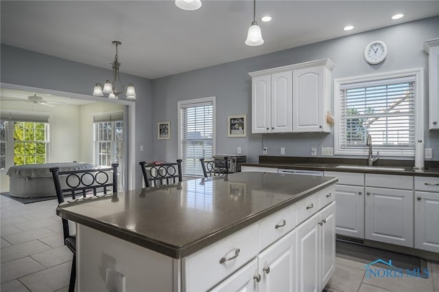 kitchen with ceiling fan with notable chandelier, sink, white cabinets, a kitchen island, and hanging light fixtures